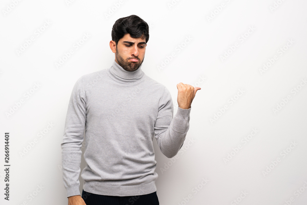 Young man over isolated white wall unhappy and pointing to the side Young man over isolated white wall unhappy and pointing to the side
