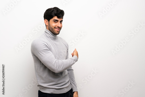 Young man over isolated white wall pointing back
