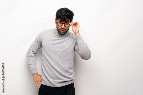 Young man over isolated white wall with glasses and surprised