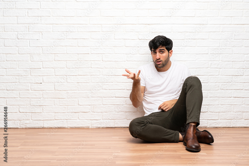 Young man sitting on the floor making doubts gesture Young man sitting on the floor making doubts gesture