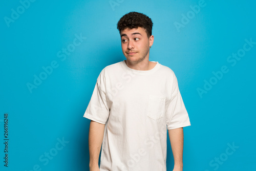 Young man over blue background making unimportant gesture