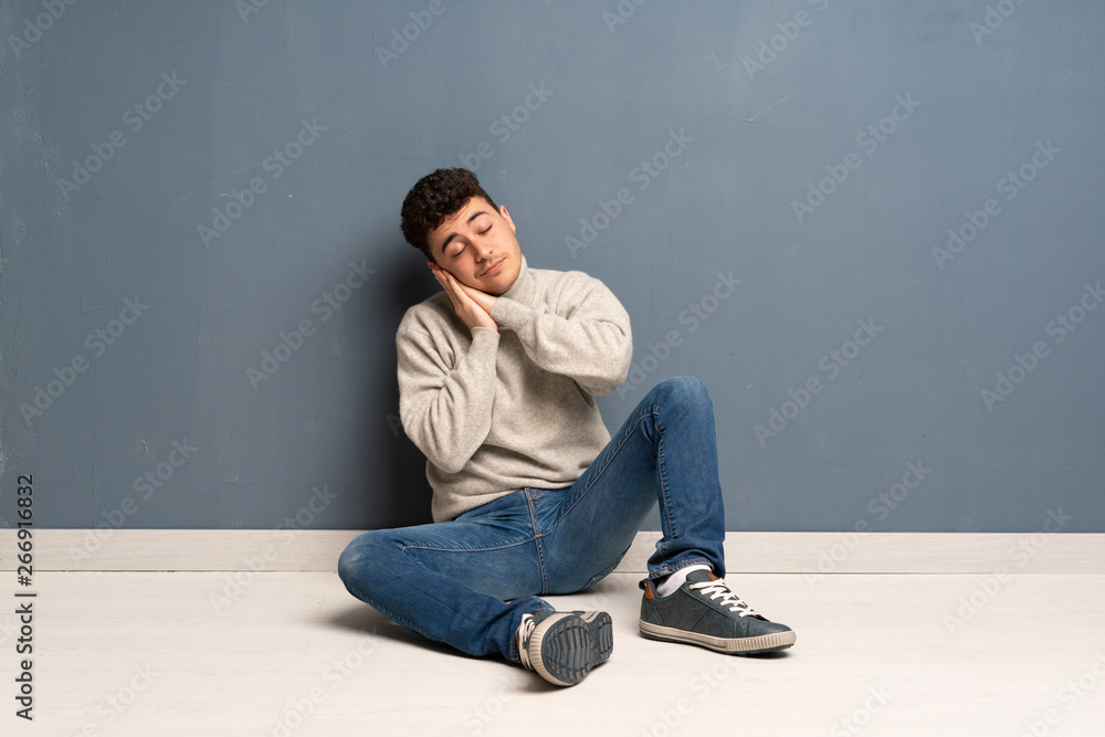 Young man sitting on the floor making sleep gesture in dorable expression Young man sitting on the floor making sleep gesture in dorable expression