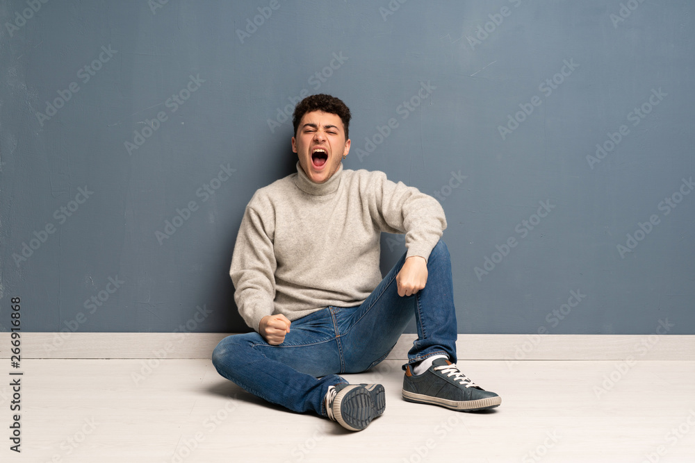Young man sitting on the floor shouting to the front with mouth wide open Young man sitting on the floor shouting to the front with mouth wide open