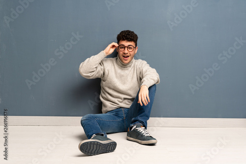Young man sitting on the floor with glasses and surprised