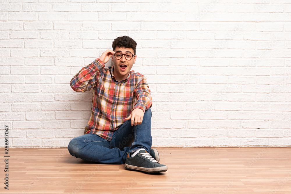 Young man sitting on the floor with glasses and surprised Young man sitting on the floor with glasses and surprised