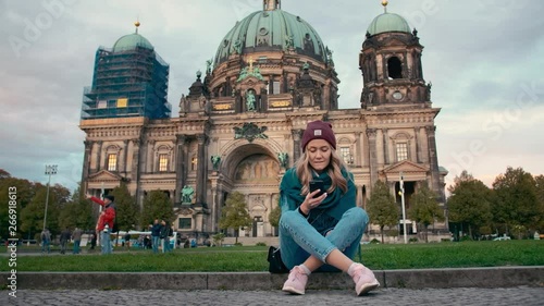 BERLIN, GERMANY - October 2018: Tourist girl in the autumn uses a mobile phone while sitting on the lawn near the cathedral in Berlin, Germany. Slow Motion.