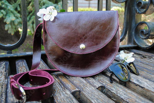 Ladies burgundy bag and sunglasses lie on a wooden bench