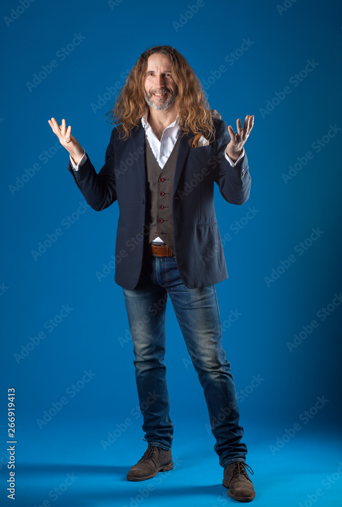 long-haired stylish man in jeans and jacket on a blue background. full-length Studio photography