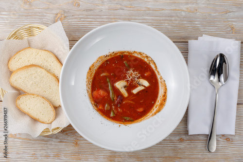 Plate of tomato soup with vegetables, bread and spoon on wooden background