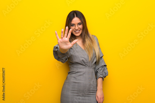 Young woman with glasses over yellow wall counting five with fingers