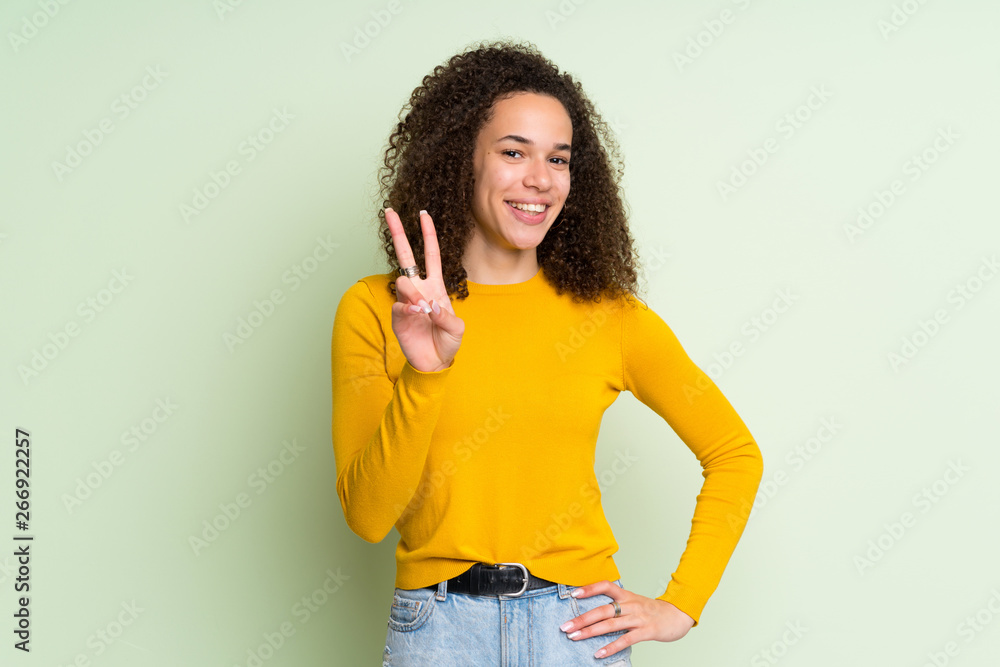 Dominican woman over isolated green background smiling and showing victory sign Dominican woman over isolated green background smiling and showing victory sign