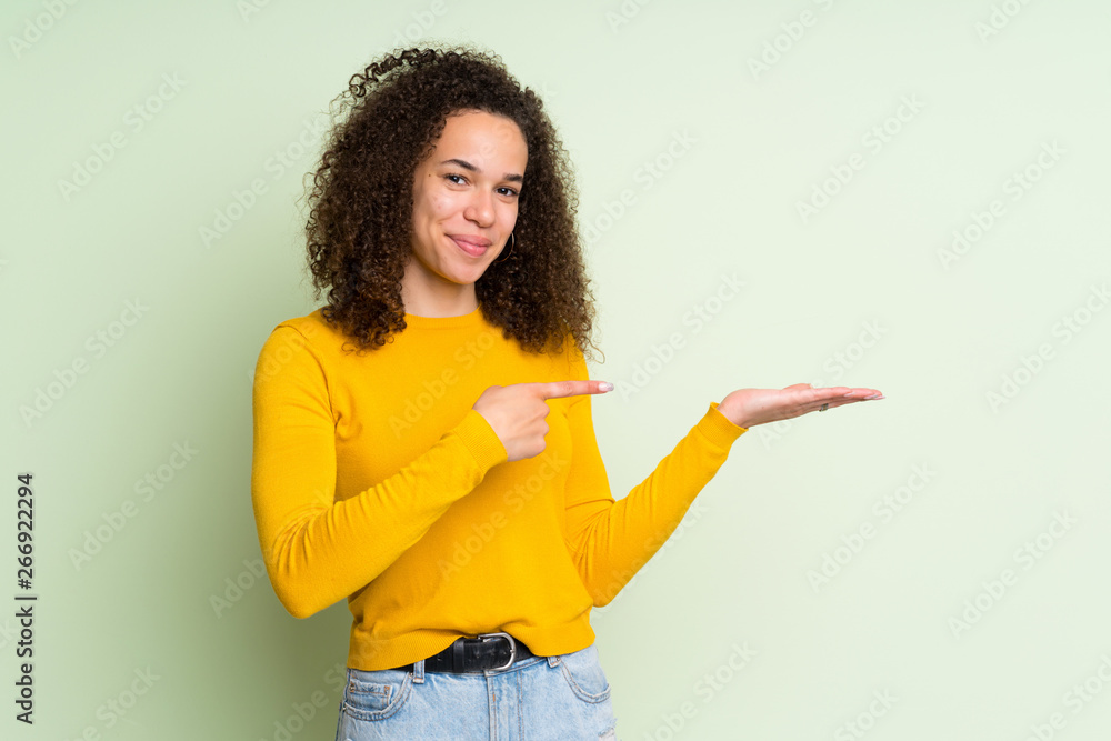 Dominican woman over isolated green background holding copyspace imaginary on the palm to insert an ad Dominican woman over isolated green background holding copyspace imaginary on the palm to insert an ad