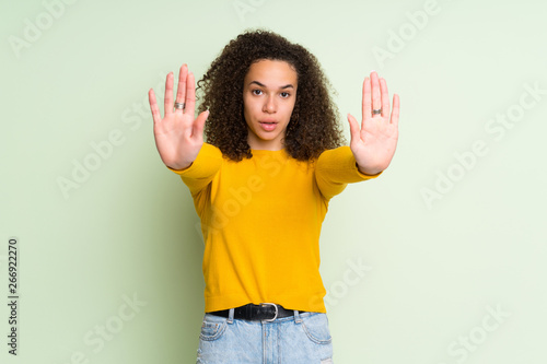 Dominican woman over isolated green background making stop gesture and disappointed