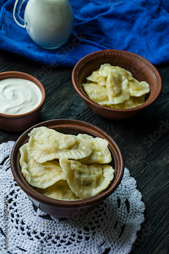 Dumplings with potatoes and cabbage. Sour cream, milk and greens. Traditional dish of Ukraine. Dark wooden background.