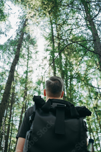 Hiker with backpack in a beautiful green forest with sunlight, climbing and looking up confident 