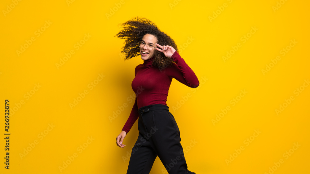 Dominican woman with curly hair jumping over isolated yellow wall Dominican woman with curly hair jumping over isolated yellow wall