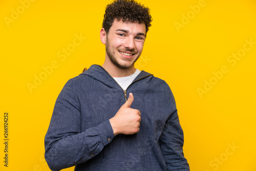 Quadro su tela Young man over isolated yellow wall giving a thumbs up gesture