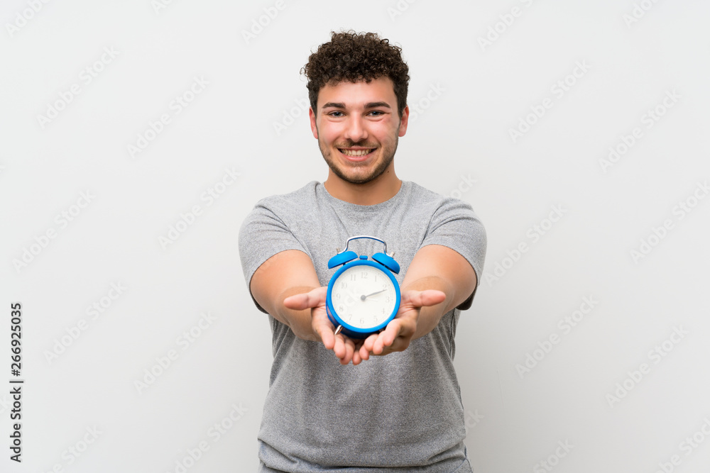 Man with curly hair over isolated wall holding vintage alarm clock