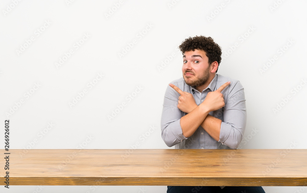 Young man with a table pointing to the laterals having doubts Young man with a table pointing to the laterals having doubts
