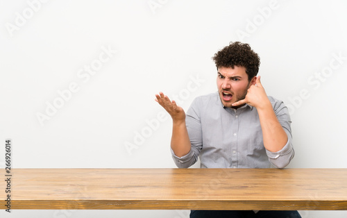Young man with a table making phone gesture and doubting