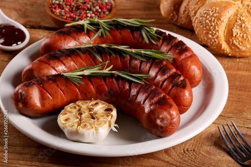 Grilled sausages with vegetables, spices and bread in white plate on wooden table