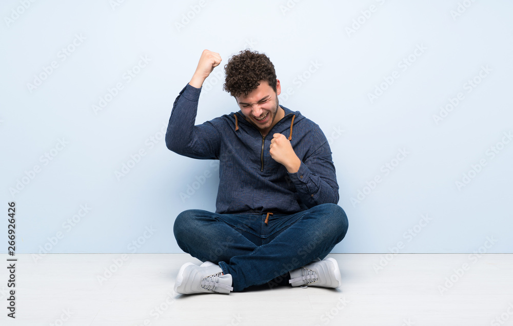 Young man sitting on the floor celebrating a victory Young man sitting on the floor celebrating a victory