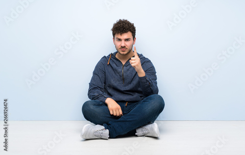 Young man sitting on the floor frustrated and pointing to the front © luismolinero