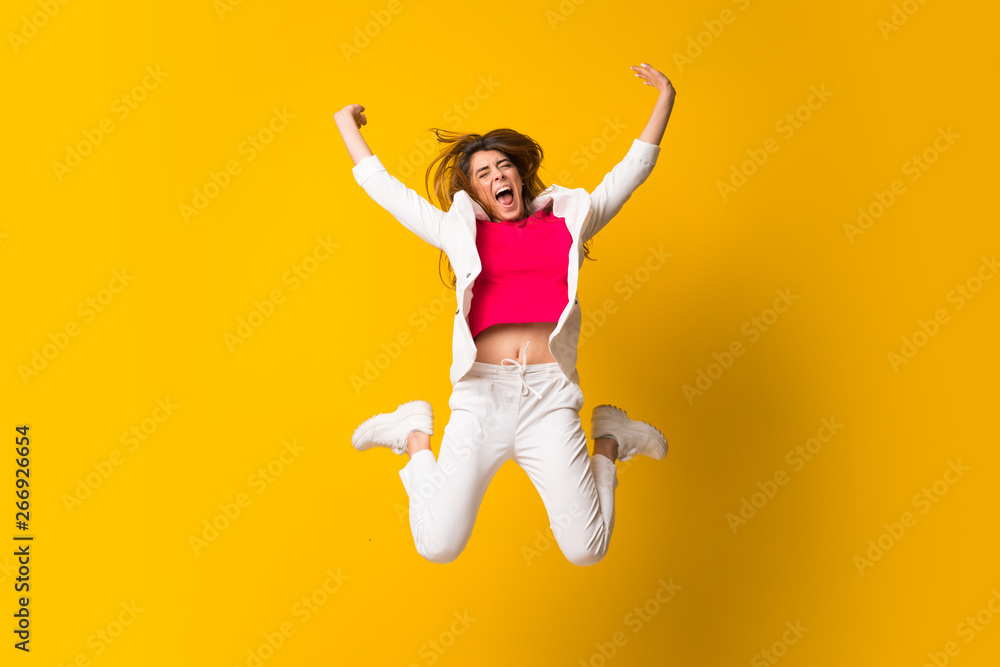 Young woman jumping over isolated yellow wall