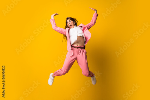 Young woman jumping over isolated yellow wall making victory gesture © luismolinero