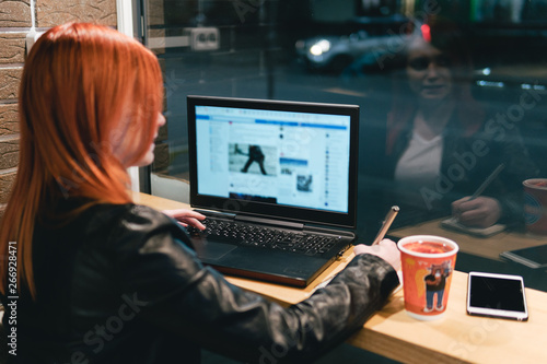 Businesswoman, girl holding a pen, writing in a notebook, laptop in cafe, smartphone, pen, use computer. Freelancer works remotely. Online marketing, education for adulte. Night city, dark theme. tea