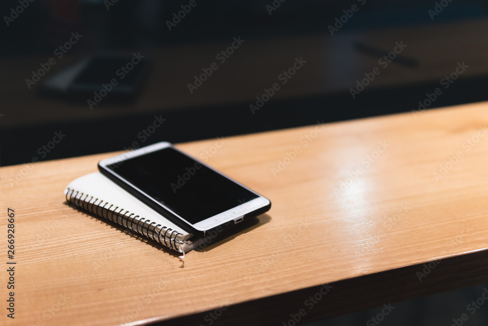 white smartphone, notebook. wooden table in cafe, Freelancer works remotely. Online marketing, education for adulte. Night city, dark theme. white smartphone, notebook. wooden table in cafe, Freelancer works remotely. Online marketing, education for adulte. Night city, dark theme.