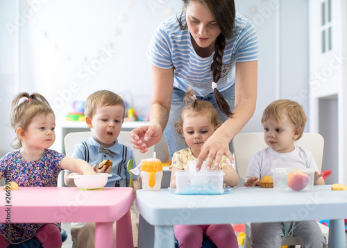 Group of nursery babies toddlers eating healthy food lunch break together with kindergartener