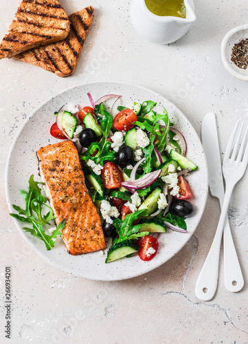 Healthy balanced lunch - grilled red fish fillet salmon and tomatoes, cucumbers, olives, feta Greek salad on a light background, top view
