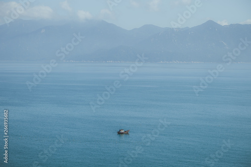 View of one boat in a blue endless bay in Vietnam with mountains in the background on a sunny day