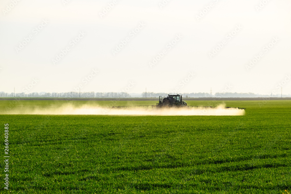 tractor with the help of a sprayer sprays liquid fertilizers on young wheat in the field. tractor with the help of a sprayer sprays liquid fertilizers on young wheat in the field.