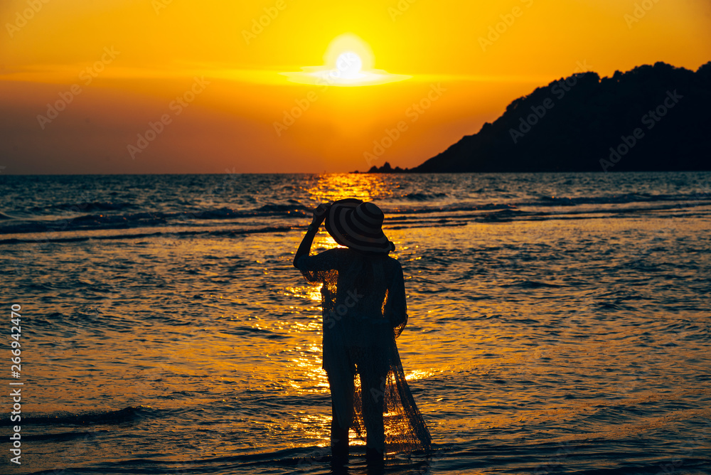 A young woman stands on the beach during a sunset, summer vacation.