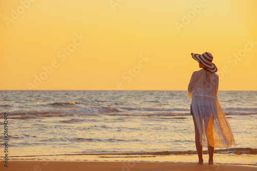 A young woman stands on the beach during a sunset, summer vacation.