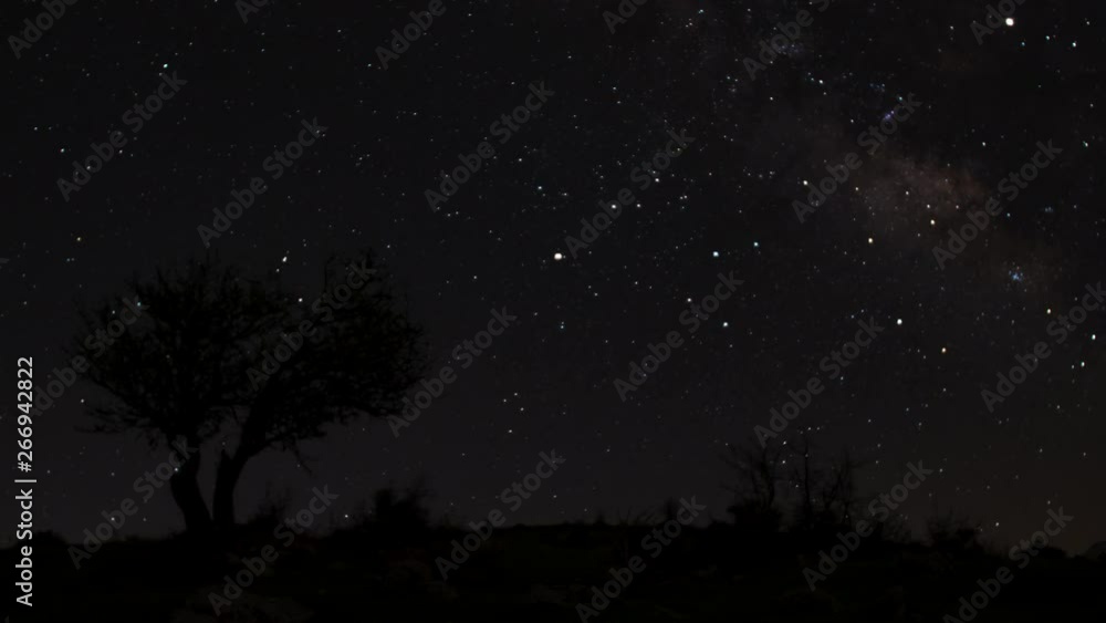Astrophotography night to day time lapse of the milky way view from a mountain. Olive tree and rocks in the foreground. Moon rising before the sun. Shadows moving on the green grass. Astrophotography night to day time lapse of the milky way view from a mountain. Olive tree and rocks in the foreground. Moon rising before the sun. Shadows moving on the green grass.