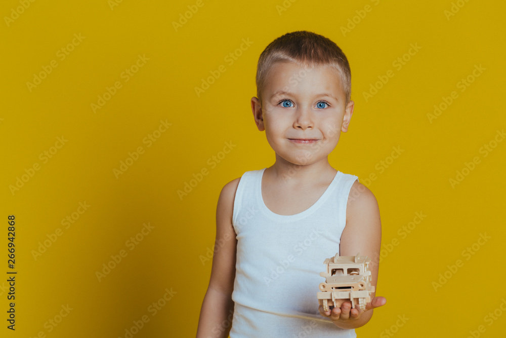 Portrait of an attractive boy in a white t-shirt playing wooden toys on a yellow background Portrait of an attractive boy in a white t-shirt playing wooden toys on a yellow background