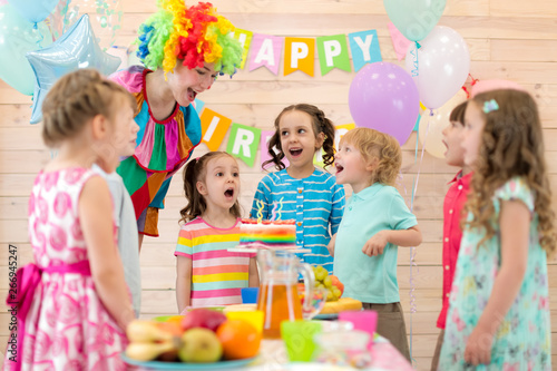 Group of kids with clown blowing candles on cake at birthday party