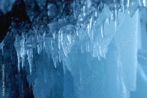 view from  ice cave. frozen, crystal clear water drops like stalactites hang from the ceiling. rising sun stained ice. partially tinted photo. focus on a central object. Extra shallow depth of field.