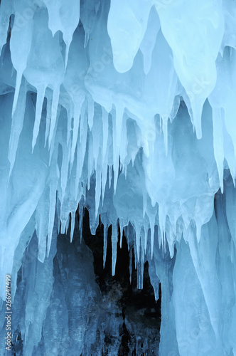 view from  ice cave. frozen, crystal clear water drops like stalactites hang from the ceiling. rising sun stained ice. partially tinted photo. focus on a central object. Extra shallow depth of field.
