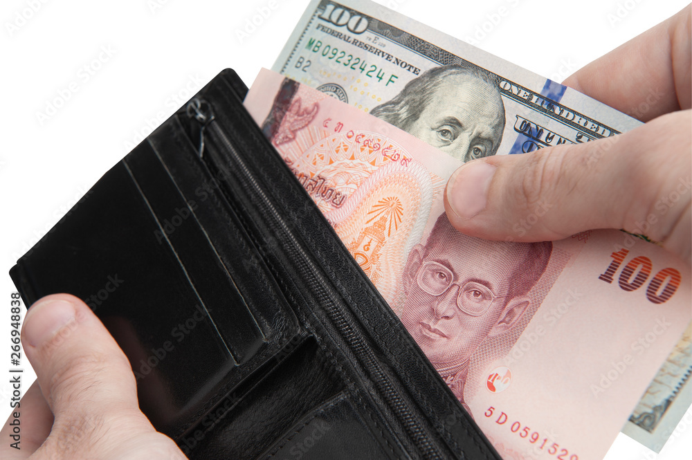 Exchanging money. Counterfeit money problem. Hand taking out 100 dollar and 100 baht banknotes from black leather wallet isolated on white background. Exchanging money. Counterfeit money problem. Hand taking out 100 dollar and 100 baht banknotes from black leather wallet isolated on white background.