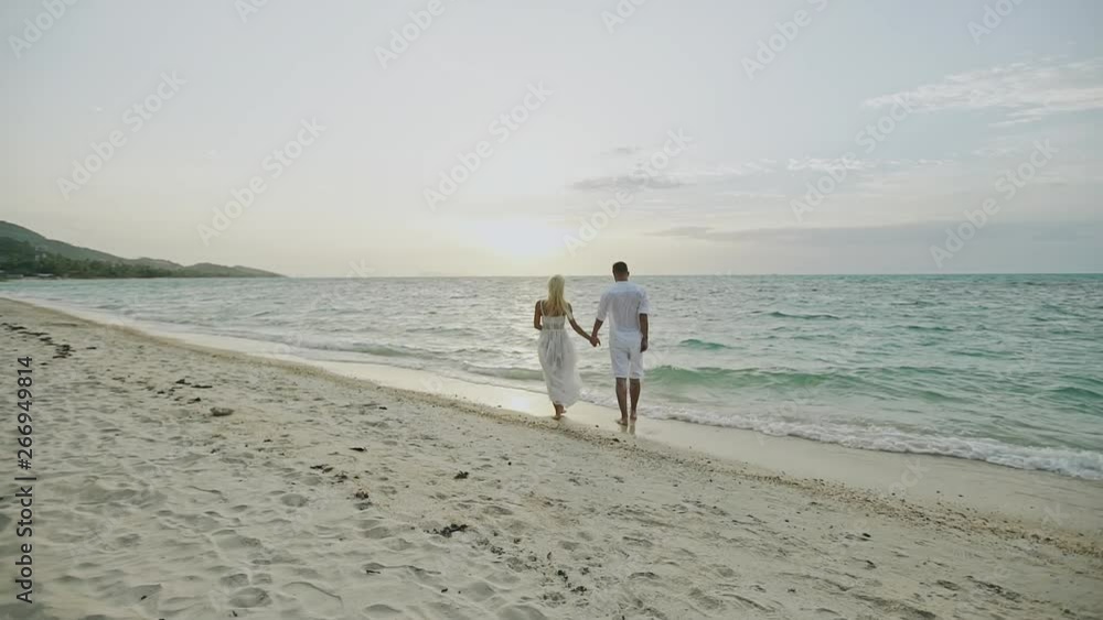 Honeymoon at the sea. Back view of loving couple walking away at sandy beach - slow motion. Honeymoon at the sea. Back view of loving couple walking away at sandy beach - slow motion.