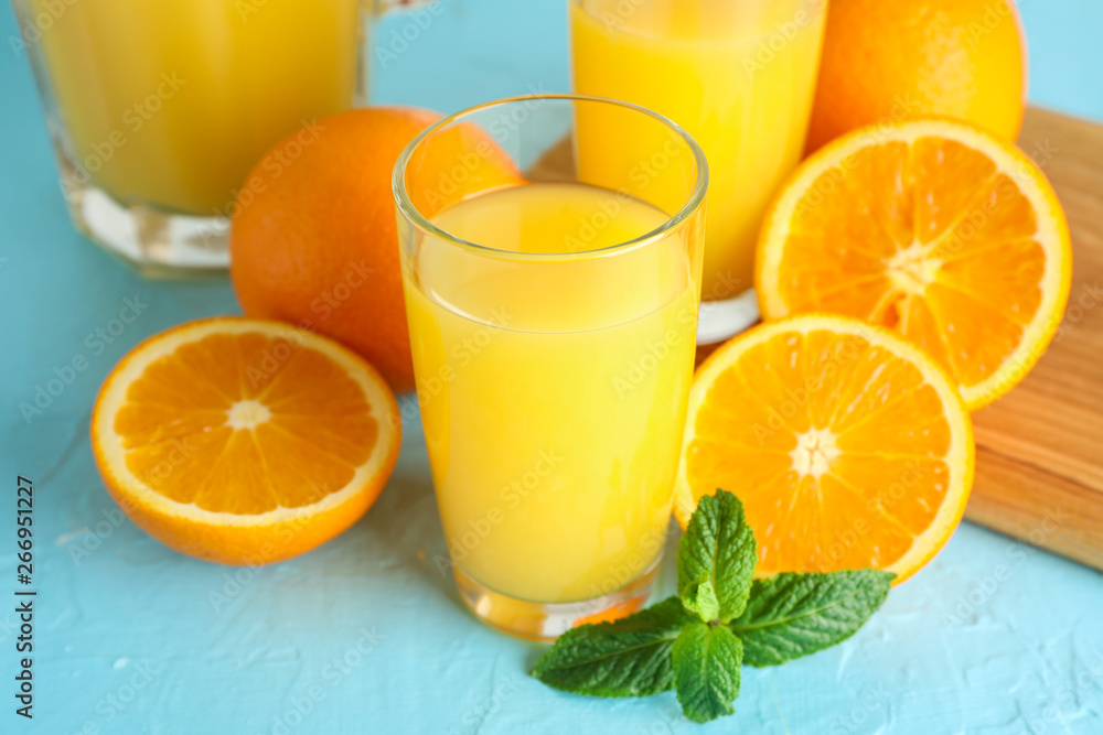 Composition with fresh orange juice in glassware, mint, and oranges on color background, closeup. Fresh natural drink Composition with fresh orange juice in glassware, mint, and oranges on color background, closeup. Fresh natural drink