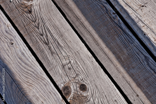 grey, worn, old and cracked wood planks of a boardwalk which have been exposed to weather and sun for years and which show knots and growth rings on the surface
