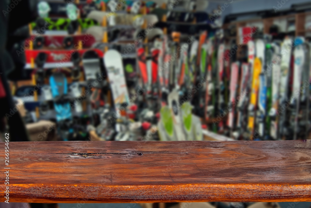 Mockup. Image of sport store with equipment for skiing. Defocused, blurred image. In the foreground is the top of a wooden table, counter. Mockup. Image of sport store with equipment for skiing. Defocused, blurred image. In the foreground is the top of a wooden table, counter.