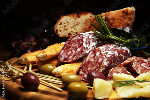 antipasto various appetizer. Cutting board with salami, cheese, bread and olives on dark wooden background