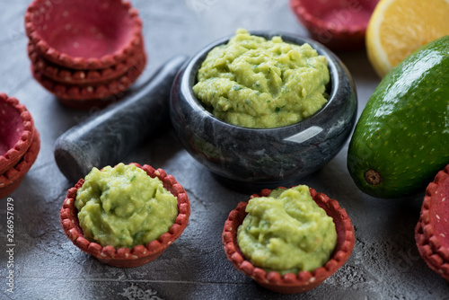 Marble mortar and red tartlets with guacamole dip, studio shot on a grey concrete surface, close-up