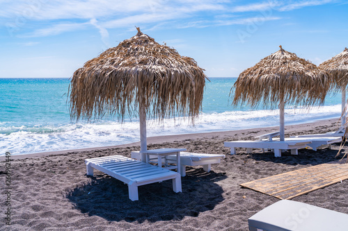 Empty deck chairs and umbrellas on the black sand beach in Perissa  Santorini  Greece